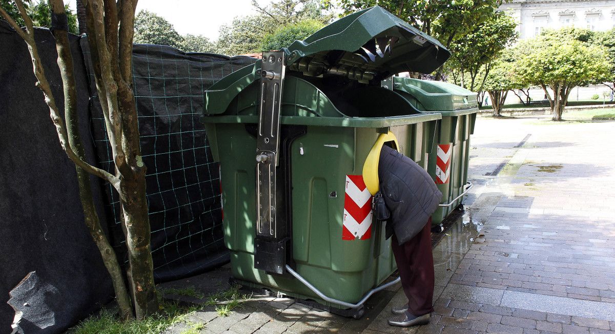 Una persona buscando en el contenedor de basura