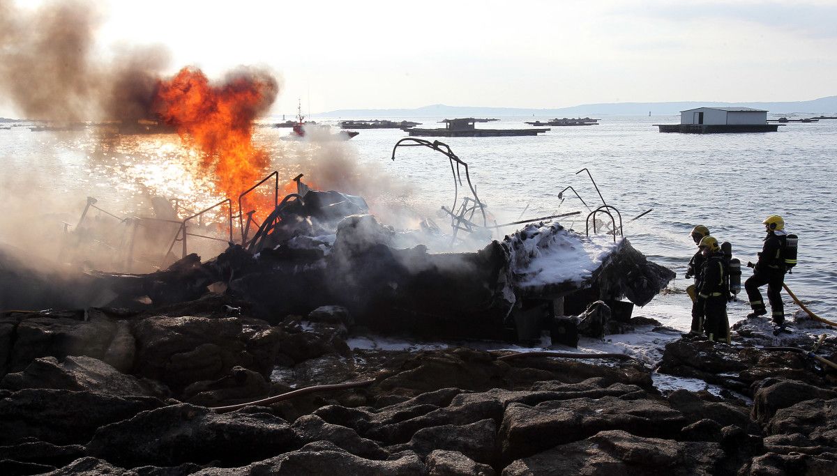 Tarefas de extinción do incendio no catamarán 'Boramar', totalmente calcinado e embarrancado na Toxa