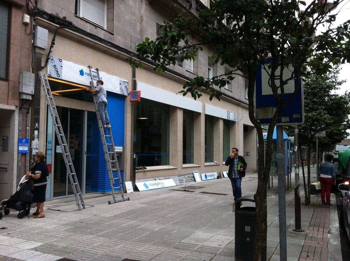 Operarios retirando los carteles de Novagalicia Banco en la sucursal de García Camba