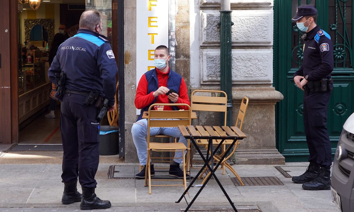 Agentes de la policía local hablan con una persona sentada en una terraza