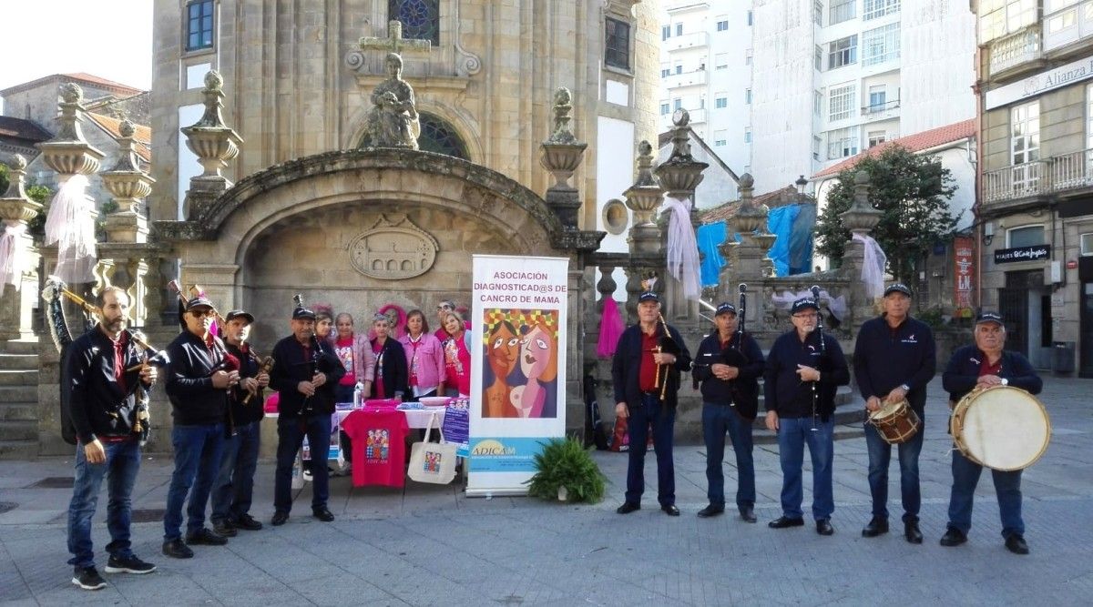 Voluntariado de Adicam e a banda de gaitas Fume de Carozo diante da mesa informativa da praza da Peregrina