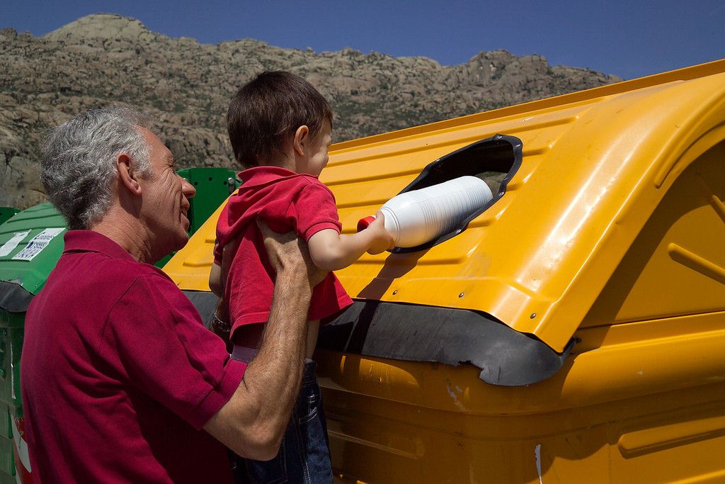 Un abuelo ayuda a su nieto a tirar un envase al contendor amarillo
