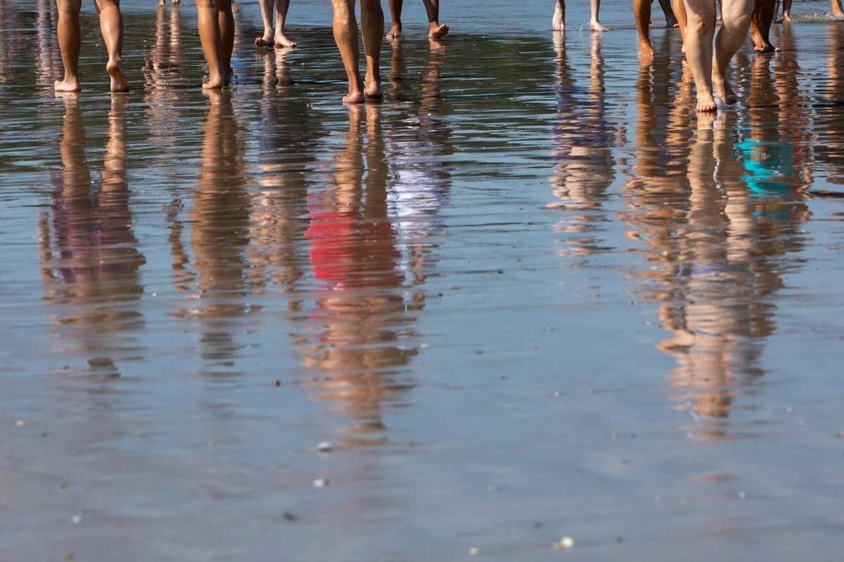 Imaxe de xente paseando pola praia reflectida na auga