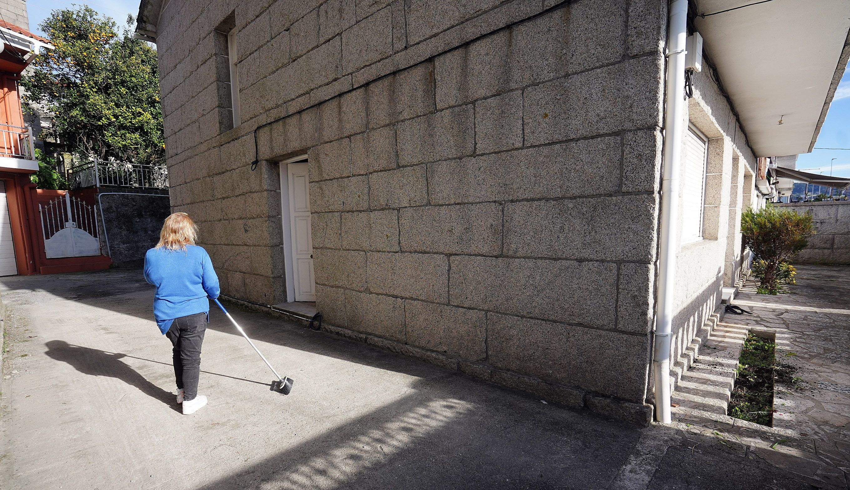 Encarnación limpia el patio delante de la puerta lateral de la vivienda por la que entraron los vecinos para desalojarlossmente unha casa en Combarro