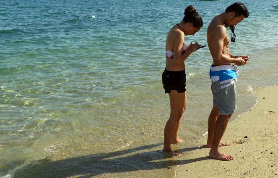 Dúas persoas na praia co seu teléfono móvil